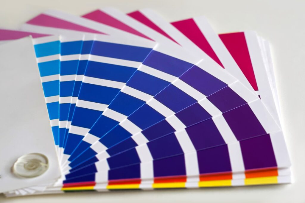 Nuancier Pantone Couleurs : Échantillons d'Impression Éventail de nuancier Pantone ouvert montrant des variations de couleurs allant du bleu clair au magenta foncé, avec bandes blanches et repères CMJN.