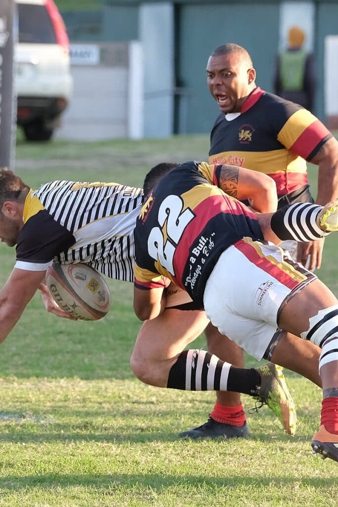 Rugby action : Mêlée intense et émotion lors du match. Rugby players tackling on a green field during a match in South Africa, showing athleticism and teamwork.