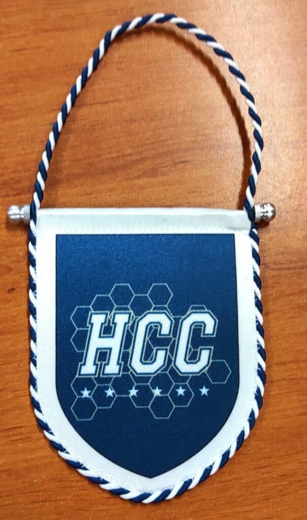 Fanion bleu HCC avec motif nid d'abeille, étoiles et bordure torsadée blanche et bleue sur fond bois.