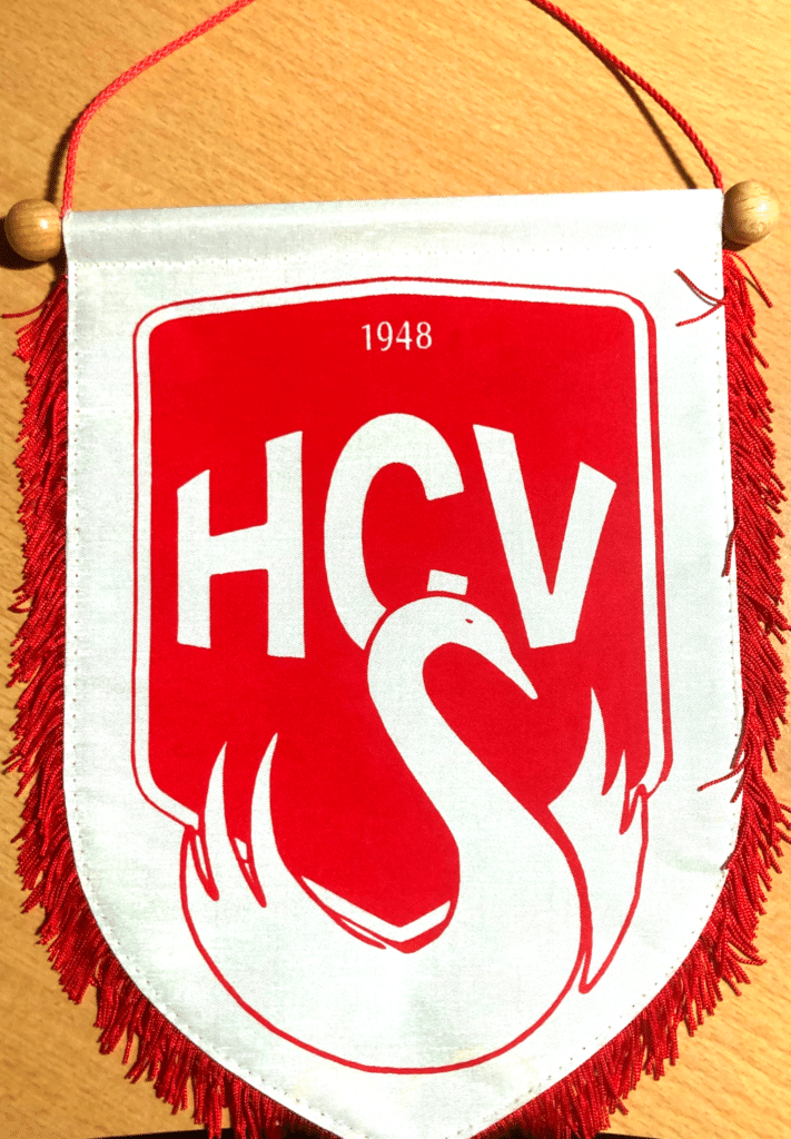 Fanion rouge et blanc avec logo HCV 1948 et cygne stylisé, bordé d'une frange décorative à fils rouges.