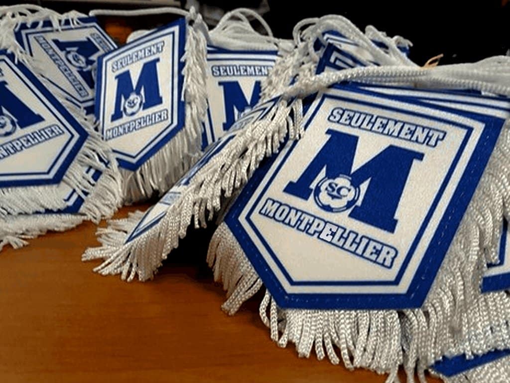 Fanions bleus et blancs marqués 'Seulement Montpellier' avec un grand M et des franges sur une table en bois.